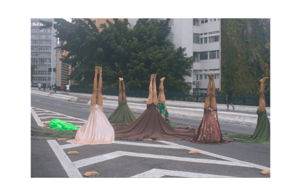 A picture of people headstanding on a road, they are wearing dresses which are falling to the ground with gravity. They look like trees.